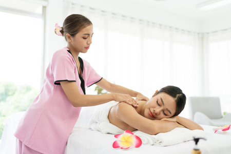 Relaxing young Asian woman lying down and closing her eyes on massage beds while receiving a massage from a therapist at an Asian luxury spa salon and a wellness center, waiting for Spa salon conceptの写真素材