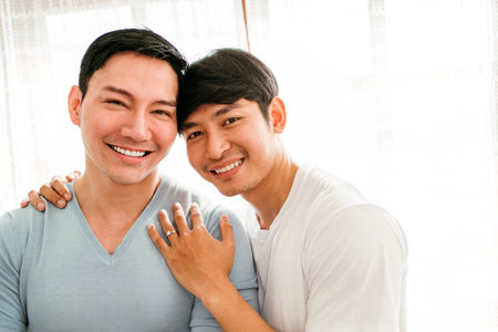 Young happy gay couple in love, proposing and marriage surprise show a wedding ring in the living room at home. Gay men proposal engagement concept. Surprised partner is very happy. Relationship goal.の写真素材