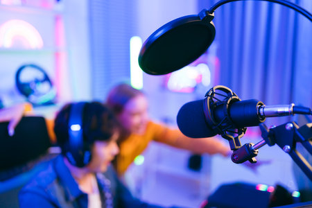 Close-up professional microphone with filter with blur teenager man and woman professional gamer prepare for competition in the background, for casting gameplay or recording a podcast.の写真素材