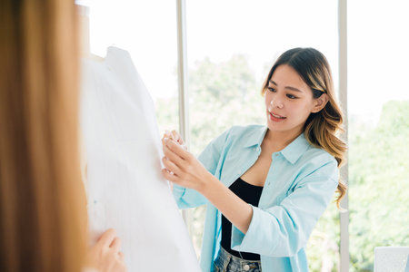 Asian woman tailor measures the mannequin to make new clothes. Attractive female fashion designer dressmaker working and designing new fashion collections for customers in an atelier tailor workshop.の写真素材