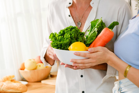 Close-up hands of a Caucasian happy couple stand in the kitchen holding a bowl with fresh vegetables...