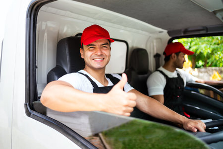 Happy professional truck driver with his assistant wearing a red cap thumb up, smiling, looking at the camera from a truck window before delivering parcel. A truck driver and delivery service concept.の写真素材
