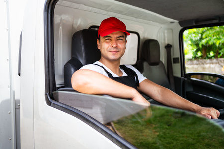 Happy professional truck driver with his assistant wearing a red cap, smiling, looking at the camera from a truck window before delivering parcel. A truck driver and delivery service concept.の写真素材