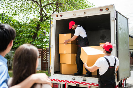 Asian and Caucasian workers in uniform unloading cardboard boxes from the truck. Delivery men...