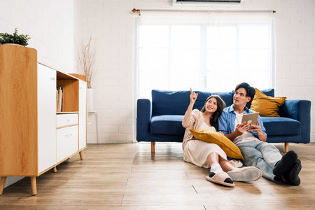 Attractive new marriage man and woman sit on the floor together in the living room and point on copy space at the new home. A family spends quality time together after moving into a new home.の写真素材