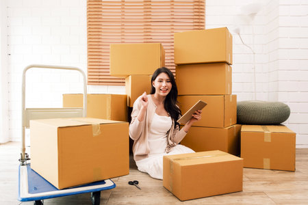 Happy Asian couple moving to a new house, Woman unboxing cardboard boxes from the old house while...