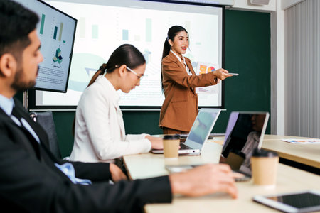 A cheerful and confident Asian businesswoman stands, present bar charts data from projector screen to her office colleagues. Asian business women leader role at the meeting.の写真素材