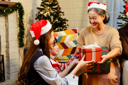 Happy and cheerful Asian family gathering, wearing Santa hats talking and smiling. Exchanging gifts, grandparents, grandchildren, daughters, sitting at the fireplace with decorated Christmas tree.の写真素材