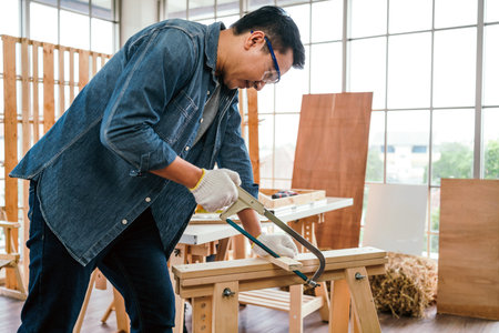 Asian father and son work as a woodworker or carpenter, Father wears safety goggles and saw a wooden...