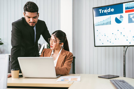 A cheerful and confident Asian businessman stands in the back and points at his businesswoman office...