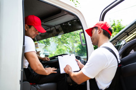 Happy professional truck driver with his assistant wearing a red cap smiling and talking about the parcel with checklists and location to deliver. A truck driver for home mover and delivery conceptの写真素材