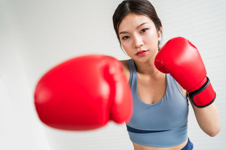 A focused woman practices boxing, wearing red gloves and a blue tank top, emphasizing strength and determination in her training.の写真素材