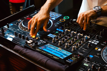 A DJ skillfully manipulates a mixing console, blending tracks to create an electrifying atmosphere at a lively event. DJ mixer controller panel for playing music and partying.の写真素材