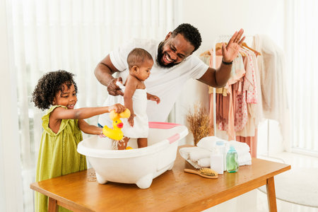 A joyful family scene of a father playfully bathing his baby, assisted by a smiling older sibling, in a bright, airy room. Happy diversity family concept.の写真素材