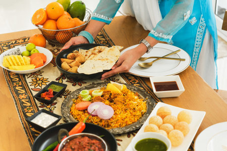 Beautifully hand arranged spread of colorful Indian traditional dishes, including Chapati, Nan, Curry, Samosa, Birjani, Panpuri and assorted fresh fruits, served on a decorative tablecloth.の写真素材