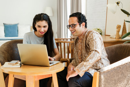 Two Indian, young woman and man adult people collaborate on a laptop in a cozy setting, smiling and...