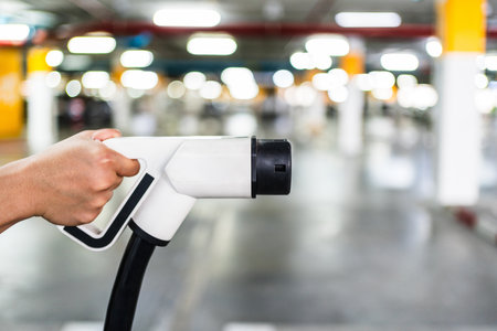 Close-up of a hand holding an electric vehicle charging plug in a parking garage. Symbolizing clean...