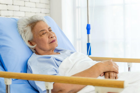 Elderly woman resting peacefully in a hospital bed, receiving medical care. The serene expression conveys comfort, recovery, and healthcare support in a clinical setting.の写真素材