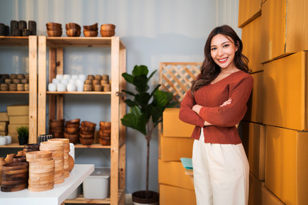 Confident female entrepreneur stands proudly in her small business studio surrounded by handmade craft products and shipping boxes, ready to grow her online store and brand presence.の写真素材