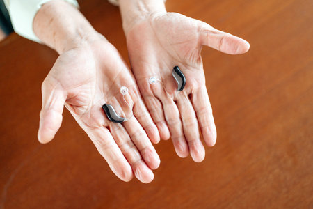 Close-up of a senior person inserting a modern hearing aid behind their ear, highlighting assistive technology, senior care, and accessibility for hearing-impaired individuals in daily life.の写真素材