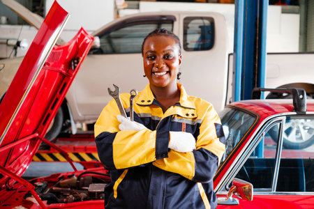 Smiling female auto mechanic in yellow and black uniform holds wrenches confidently in a repair...