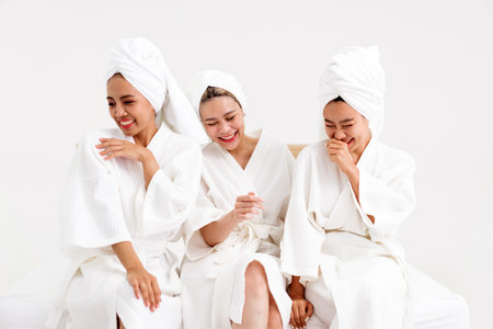 Three women in white bathrobes and towels laugh together during a spa day, capturing friendship, relaxation, and joy. Perfect for wellness, beauty, and lifestyle content with spa-related themes.の写真素材