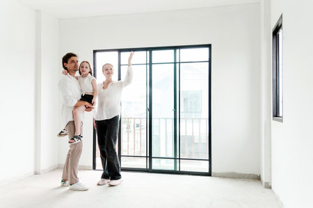 Young family standing inside a new house, envisioning their future home. Perfect for real estate, home buying, property investment, and lifestyle content showing hope and modern living.の写真素材