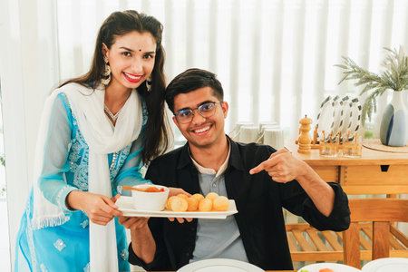 Smiling young Indian couple showcasing a plate of golgappa with chutney, celebrating traditional...