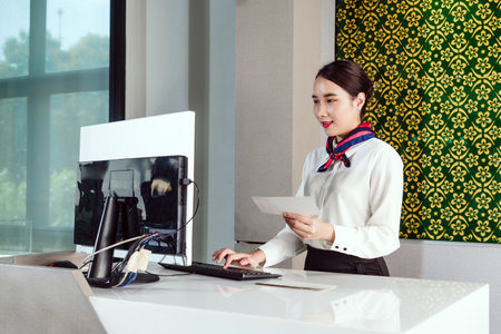 Airline ground staff in uniform processes a boarding pass at a modern check-in counter. Captures professionalism, customer service, and travel efficiency in an airport setting.の写真素材