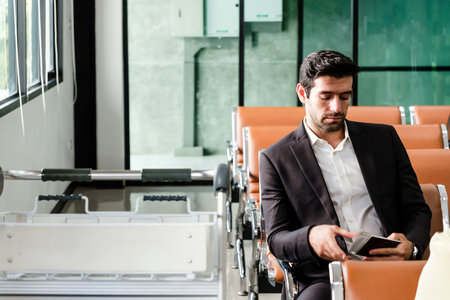 Businessman waiting at airport gate holding passport and boarding pass, dressed in a suit. Captures modern travel, airline check-in process, and professional mobility in a calm terminal setting.の写真素材