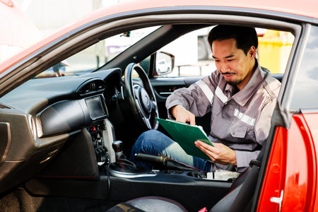 Auto service technician reviews inspection checklist inside a red car at a service center, representing professional maintenance, diagnostics, and customer-oriented automobile repair service.の写真素材