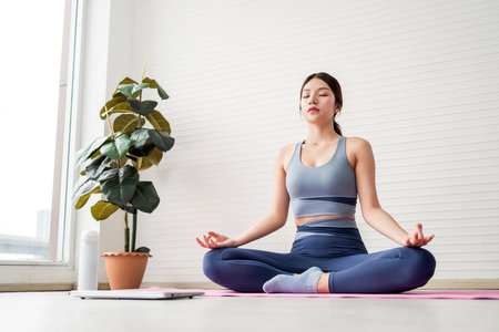 Woman in yoga pose meditating peacefully indoors on a pink mat, wearing fitness clothing, representing mindfulness, mental clarity, wellness routine, and a calm, healthy lifestyle in natural light.の写真素材