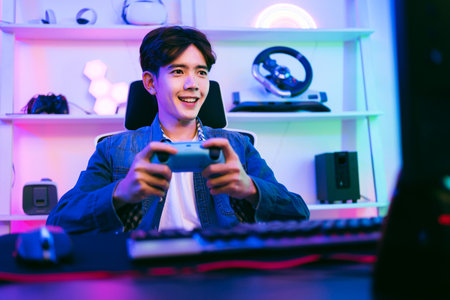 Young man enthusiastically playing video games at home with a game controller, surrounded by neon lighting and modern gear. Ideal for themes of gaming, streaming, fun, and esports lifestyle.の写真素材