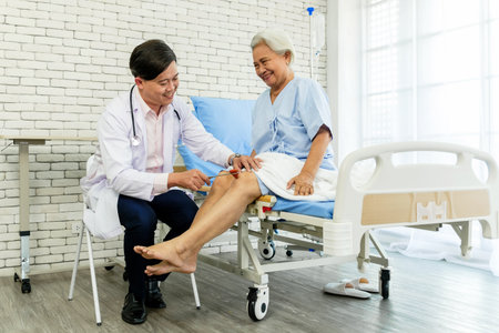 A doctor performs a reflex test on an elderly womanâs knee during a hospital checkup. The scene shows compassionate care, medical expertise, and the importance of senior health and wellness.の写真素材