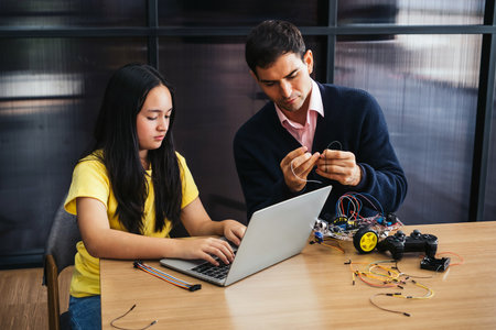 A young girl and her teacher work together on a robotics project using a laptop and controller. They focus on coding and assembling parts, encouraging STEM education and creative problem-solving.の写真素材