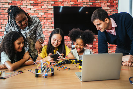 Diverse group of students learning robotics with teachers in a classroom. Smiling girls use...