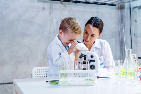 A young boy and female scientist explore plant samples under a microscope in a lab, learning eco-friendly farming technology. Promotes STEM education, sustainability, innovation in agriculture.の写真素材