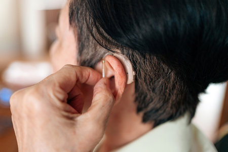 Close-up of a senior woman adjusting her hearing aid, showcasing healthcare support, assistive hearing technology, and daily independence solutions for aging and hearing-impaired individuals.の写真素材