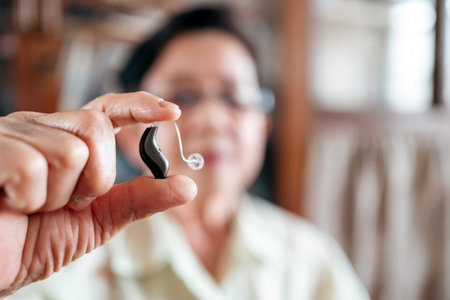 Senior woman holding a modern hearing aid device, symbolizing advanced hearing care, elderly wellness, and daily life support in healthcare for aging populations and hearing loss solutions.の写真素材
