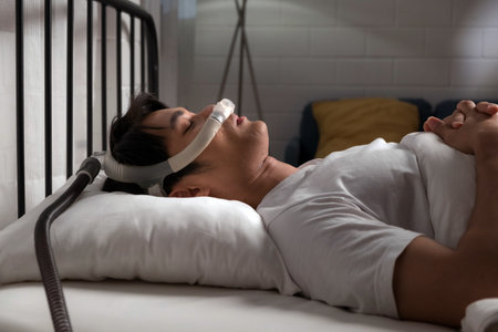 Young man sleeping with a CPAP mask for obstructive sleep apnea (OSA) and snoring relief. Nighttime use of continuous positive airway pressure therapy in a bedroom setting for better breathing.の写真素材