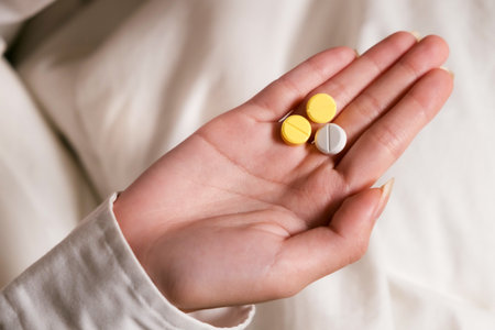 Close-up of a womanâs hand holding two yellow tablets and one white pill, symbolizing medication, treatment, or health care. Captures a personal view of daily wellness or pharmaceutical use.の写真素材