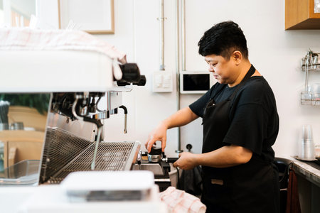 Focused barista prepares fresh coffee behind espresso machine in a cozy cafe. Daily work routine highlights dedication and quality service in small business coffee shop environment.の写真素材