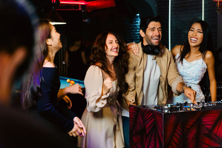 Group of young, diverse friends laugh and enjoy a vibrant night out at a club with a DJ. Happy, carefree atmosphere captured at the DJ booth with neon lights and party vibes all around.の写真素材
