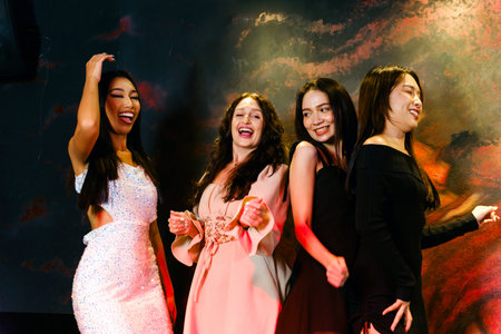 Four diverse young women in stylish outfits dance and laugh together at a nightclub. Vibrant party atmosphere with colorful lighting, energy, and friendship captured in a fun nightlife moment.の写真素材
