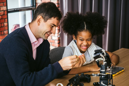 Young girl smiles as a teacher helps her explore a robotic hand model in class. Engaging in hands-on STEM learning, they focus on innovation, creativity, and practical education in technology.の写真素材
