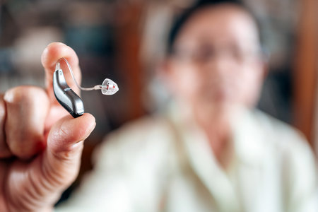 Close-up of senior woman holding modern hearing aid device. Concept of hearing loss, elderly care, and audiology. Focus on assistive technology in healthcare and daily support for older adults.の写真素材