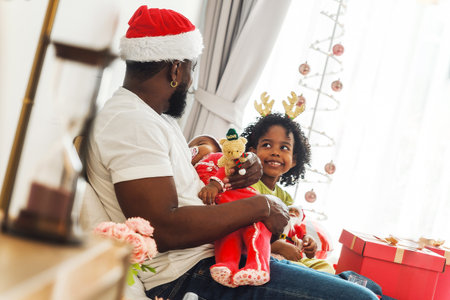 Parent and child in Santa hat and reindeer headband enjoy a festive Christmas moment by tree with gifts. Cozy holiday celebration captures family joy, warmth, and seasonal cheer in home setting.の写真素材