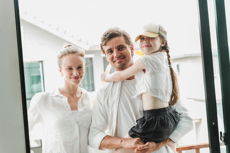 Smiling family at front door of modern home. Father holds daughter as mother stands nearby. Casual scene shows parents with child, highlighting parenting, parenthood, and happy home moments.の写真素材