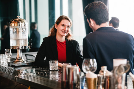 Two business colleagues network at modern hotel bar, seated across counter with glassware. Informal meeting blends corporate partnership, hospitality, and professional teamwork discussions.の写真素材