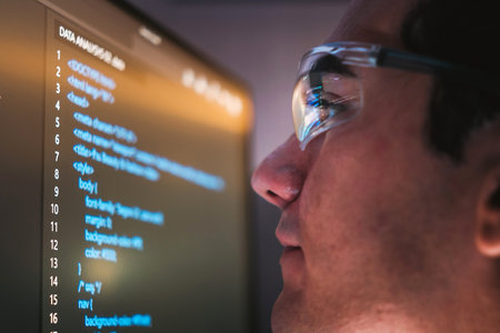 Close-up of a developer in glasses focused on a computer screen with HTML and CSS code, lens...